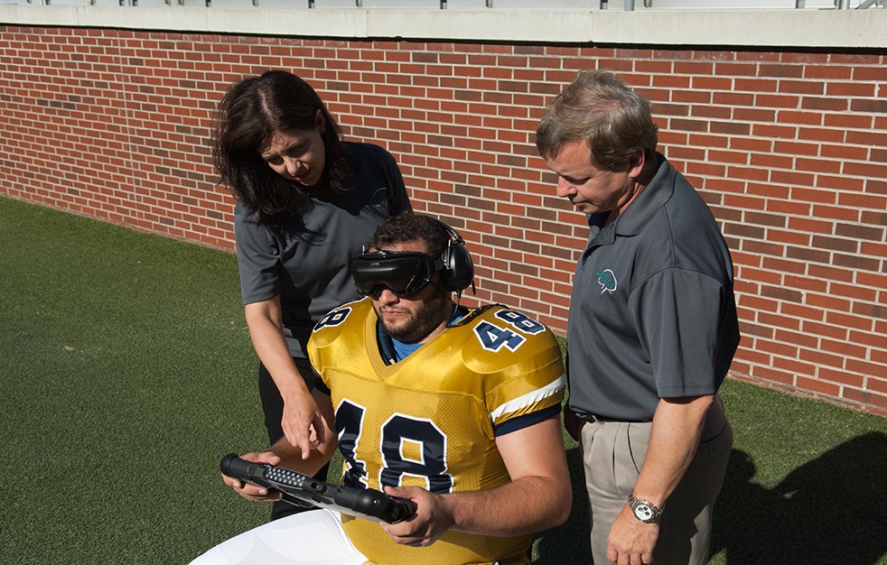 Football player with VR goggles and two engineers